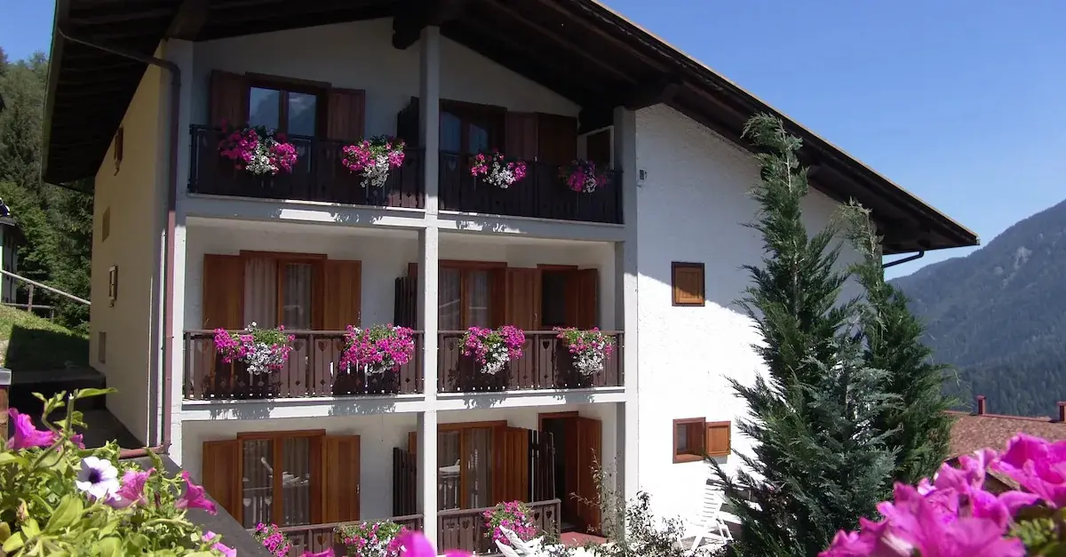 Balconi fioriti e facciata dello chalet, con il bosco sullo sfondo
